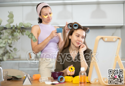 Adult woman curls hair of young woman