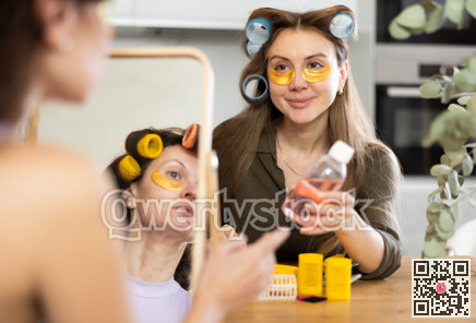 Woman in hair rollers applying eye patches in front of mirror with friend