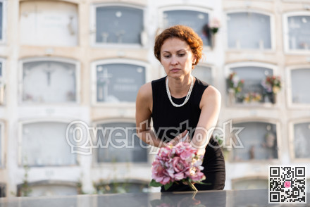 Sad widow in black lays bouquet of flowers on her dead husband grave