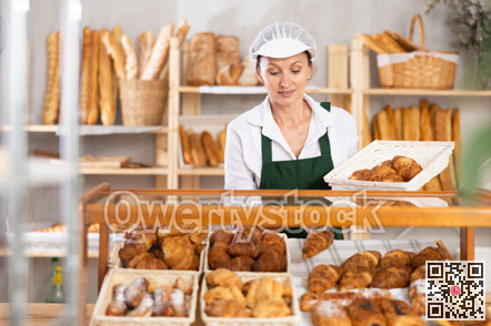 Woman employee puts croissants in window, arranges display of goods at bakery.