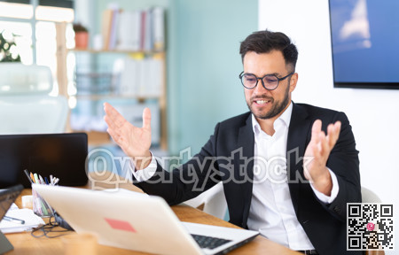 young man in glasses sits at a table and looks at a laptop screen