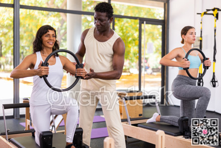 Two women having pilates workout on reformers with trainer