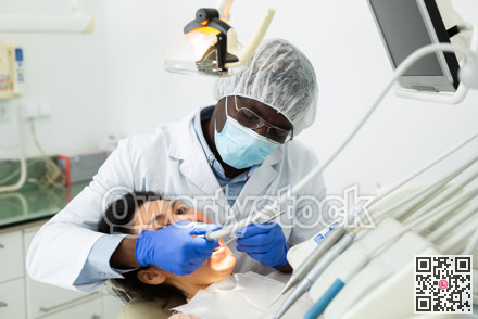 African american dentist is treating female patient which is sitting in chair
