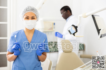 Female dentist standing in dental office with tools in hands