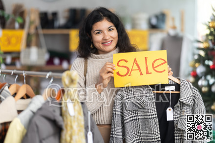 Latina woman standing in a store at a Christmas sale with a yellow poster