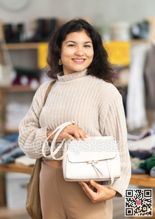 Latina woman happily chooses fashionable handbag in clothing store.