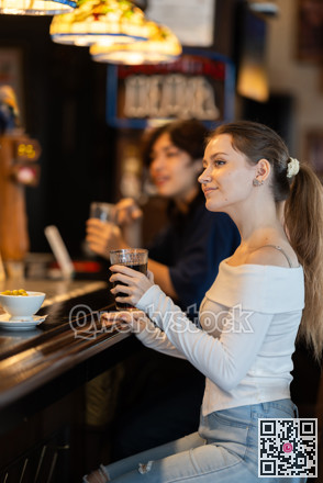 Glad young girl relaxing near bar counter and drinking alcohol in beer pub