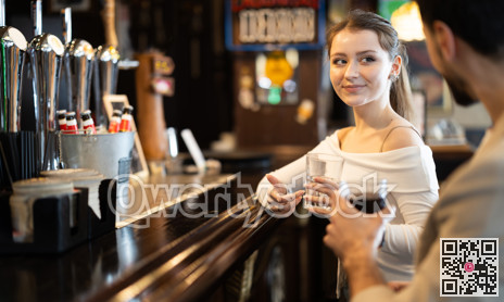 Young woman drinking beer and chatting with man at bar