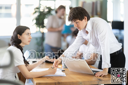 Young man showing place to sign on document to young woman filling