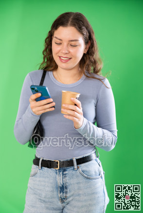 Young woman scrolling smartphone and drinking coffee in front of green screen