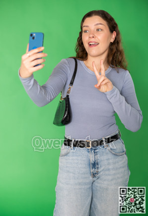 Young woman taking selfie in front of green screen