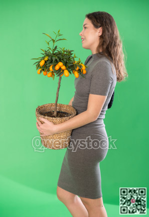 Young woman holding kumquat plant in pot in front of green screen