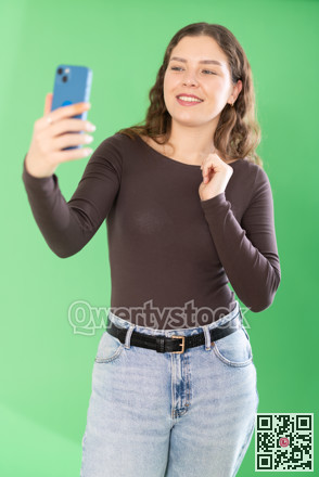 Young woman taking selfie in front of green screen