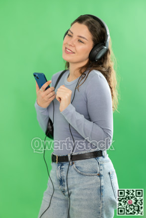 Young woman listening to music with headphones in front of green screen