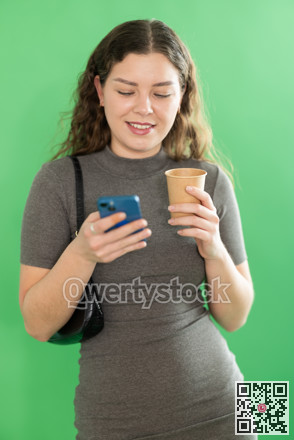 Pretty young woman scrolling through her smartphone screen against and drinking coffee green screen background. Chroma key compositing