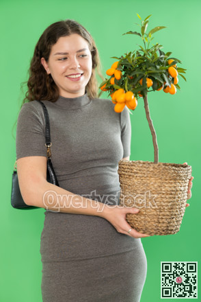 Portrait of happy girl in long dress with kumquat plant in her hands on green background