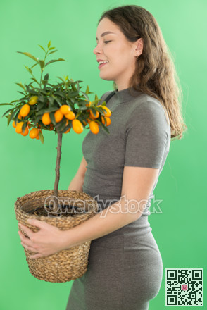 Young woman in gray dress with potted miniature kumquat in her hands