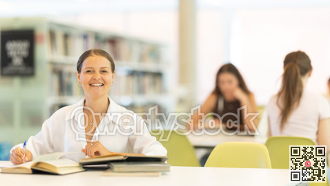 Female student sits at table in library and studies, reads books and takes notes