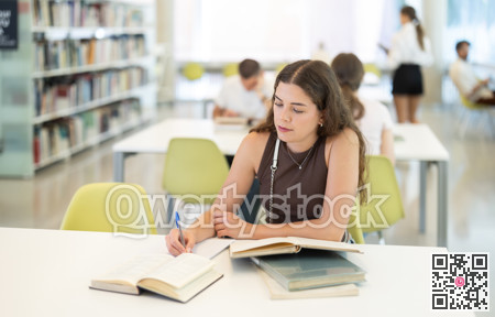 Girl reading books at table in university library - preparing for exams