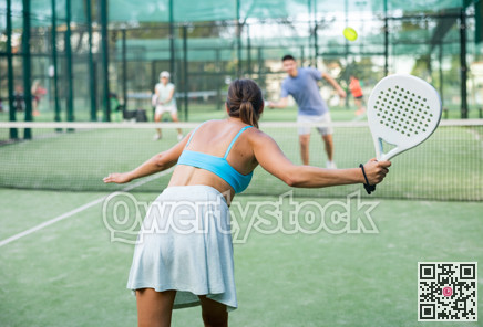 Sportive slim woman with racquet playing padel in court. View from back