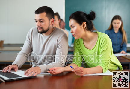 Man and woman helping each other to solve problem on laptop while studying in university class