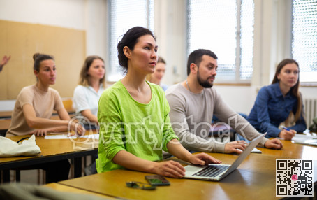 Female student writing lectures in workbooks and laptop in classroom during lesson