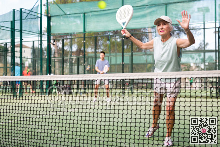 Aged woman playing friendly paddleball match on outdoor court
