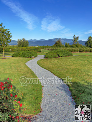 Gravel pathway over green lawn to farm orchard fields with mountains skyline