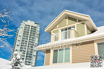 Top of residential house in snow and high-rise building on cloudy sky background